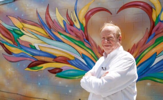 Heart attack survivor stands beside a heart mural in downtown Mansfield.