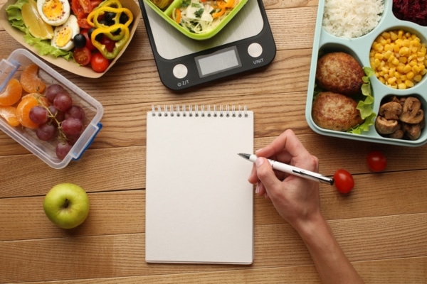 A woman writes in a food diary on a table arrayed with healthy meals.