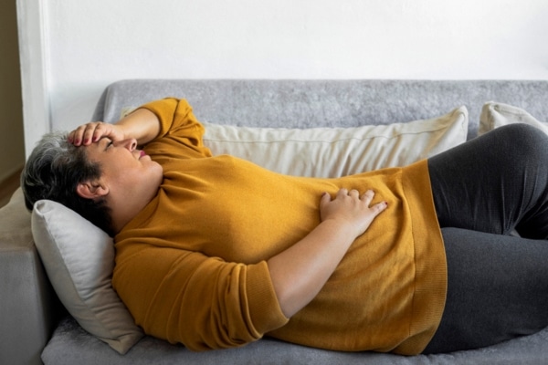 A woman lies on a couch suffering from abdominal pain from a gallstone.