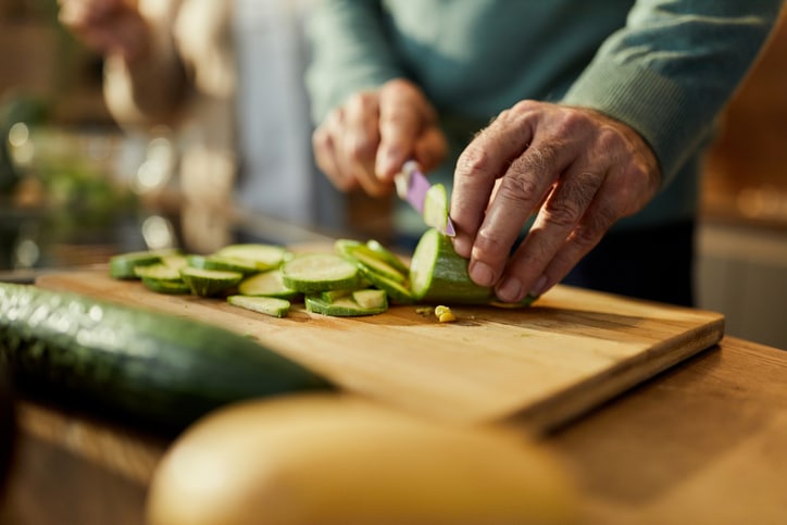 Close up of unrecognizable man cutting fresh zucchini for salad in the kitchen.