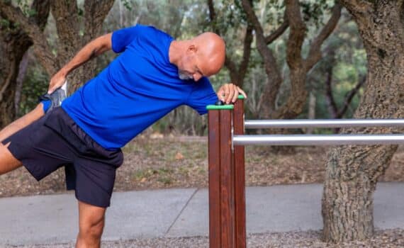 A bald middle-age man stretches his legs at a park.