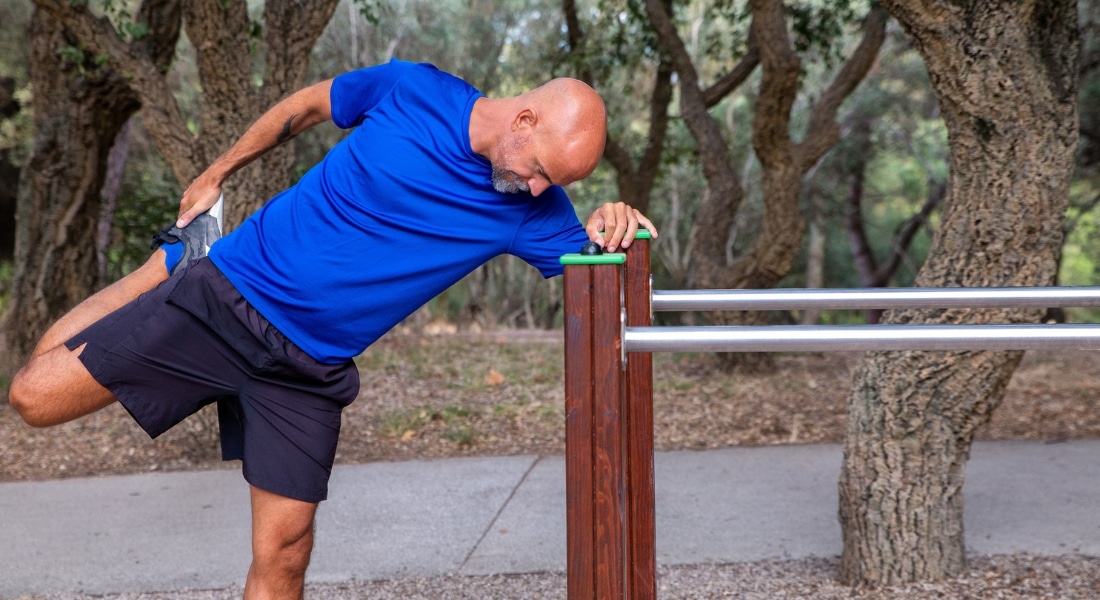 A bald middle-age man stretches his legs at a park.