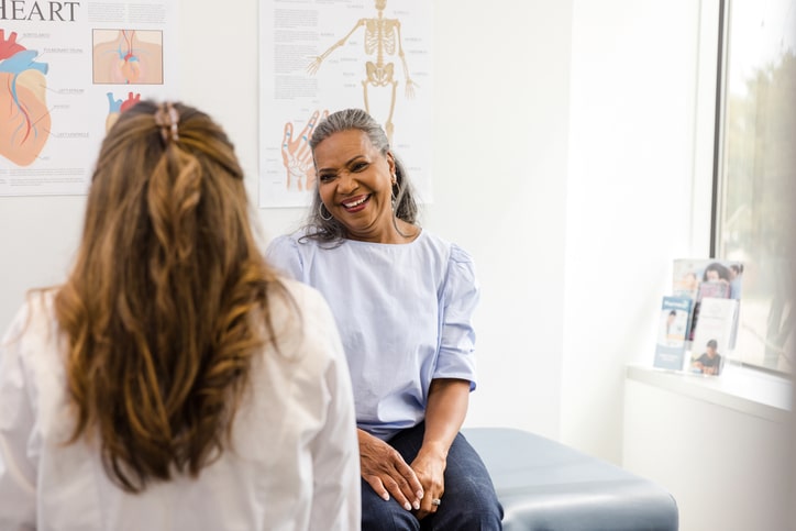 A woman smiles while listening to the doctor give her some advice.