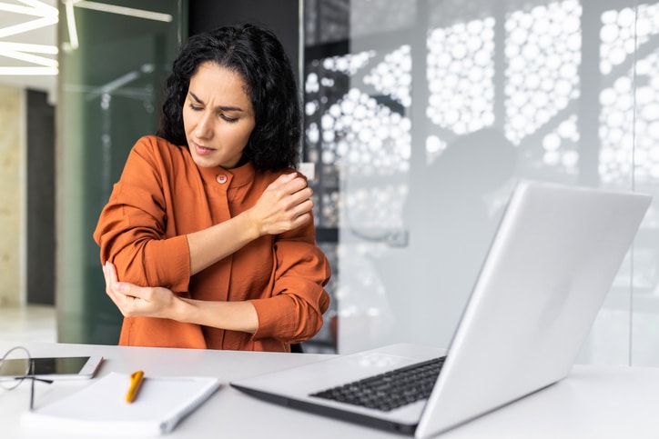 Businesswoman at the workplace sits tired and overworked, has severe pain in her hands and elbow joints.