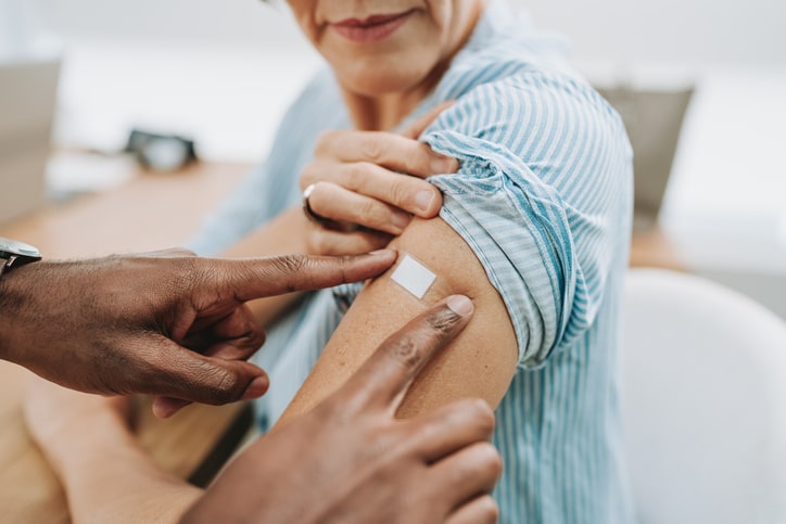 A nurse places a bandage on the shoulder of an older woman who just received a shingles vaccine.