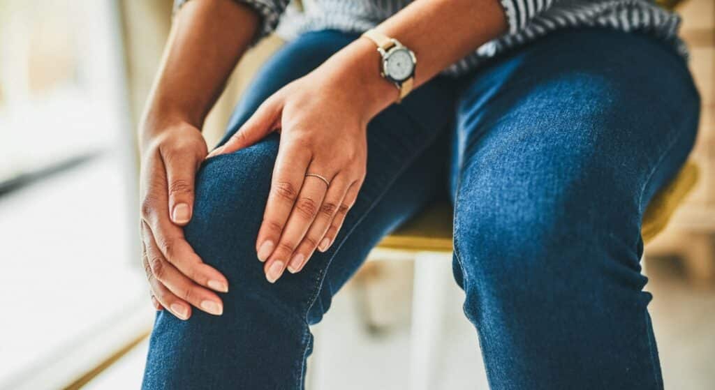 A woman rubs her knee while sitting in a chair.