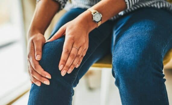 A woman rubs her knee while sitting in a chair.