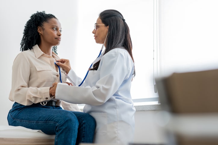 A doctor listens to her female patient's heart.