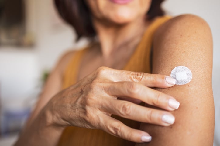 A woman in menopause sticks a transdermal patch on the skin. 