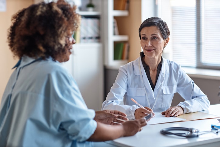 Medium shot of smiling woman gynecologist consulting African American female patient while sitting in clinic office
