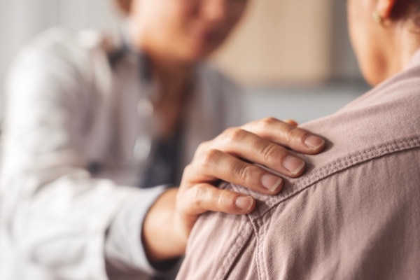 A doctor comforts a female patient with a hand on her shoulder.