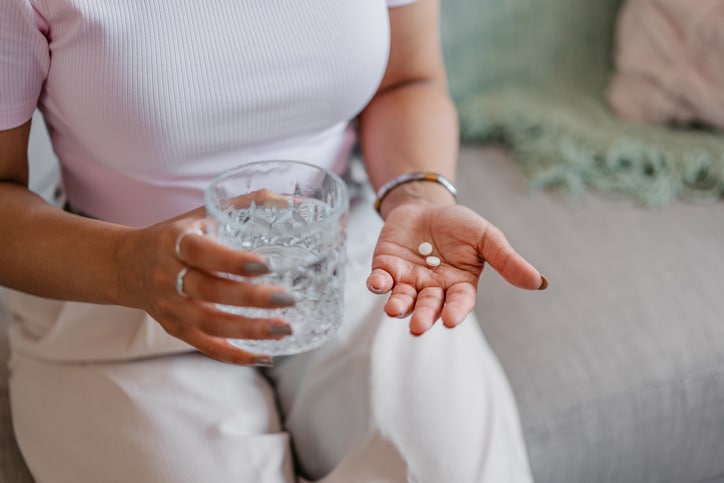A woman taking hormone therapy pills with a glass of water.
