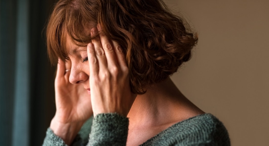 A woman in perimenopause holds her hands to her temples whole dealing with brain fog.