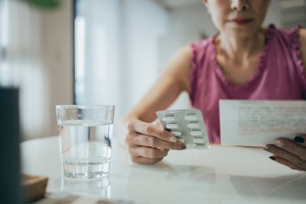 A woman reads instructions while holding a package of hormone therapy pills.