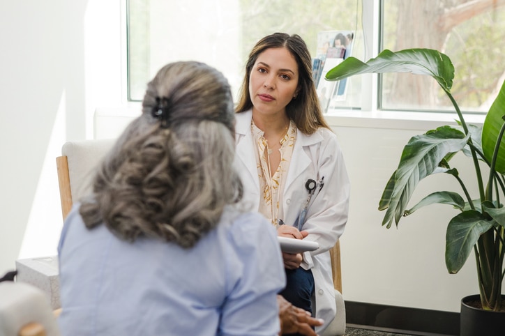 With a serious look on her face, the mid adult doctor listens carefully to the unrecognizable senior adult female patient.