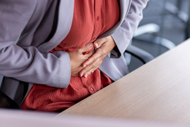 A woman sitting at a conference room table clutches her midsection while needing to use the restroom.
