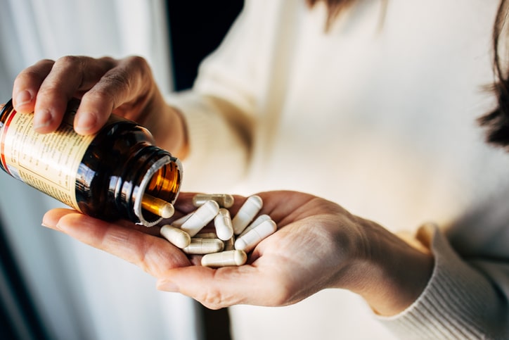Woman pouring supplement from a bottle into her hand.