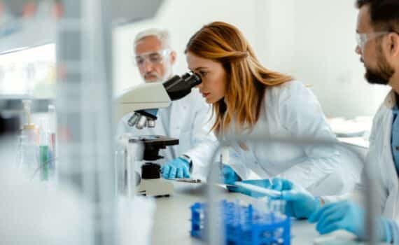 A female researcher looks into a microscope while studying the effects of hormone therapy drugs.