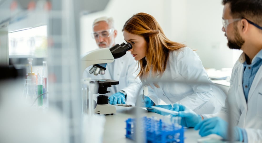 A female researcher looks into a microscope while studying the effects of hormone therapy drugs.