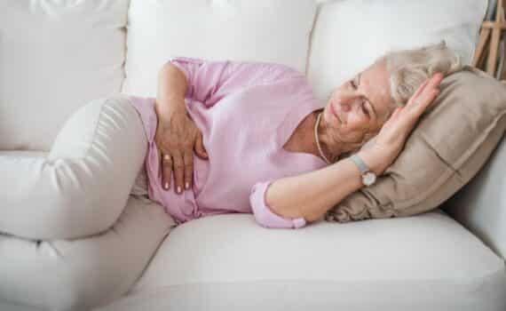 Older woman with stomach pain lies on couch in living room