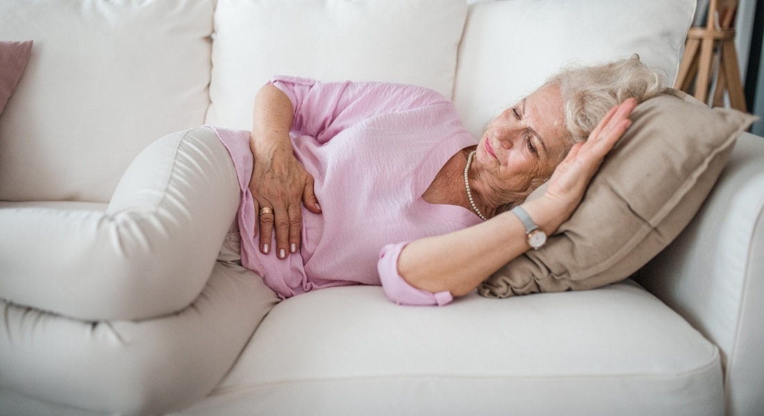 Older woman with stomach pain lies on couch in living room