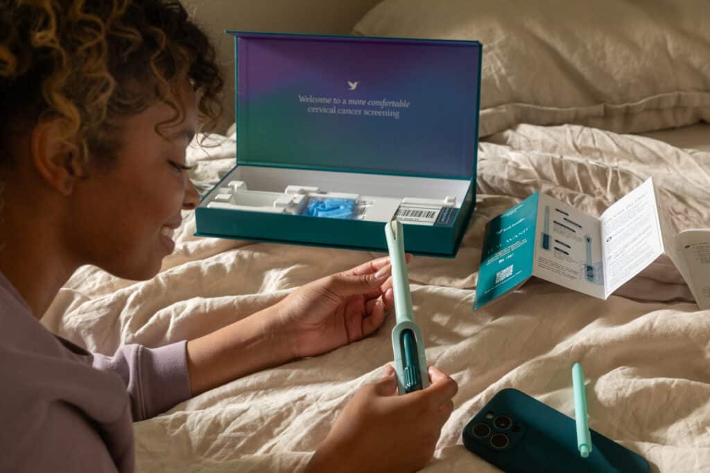 A woman unboxes the Teal Wand HPV test while lying on her bed.