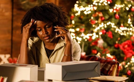 Overwhelmed young woman working for Christmas holidays, talking on the phone at her desk