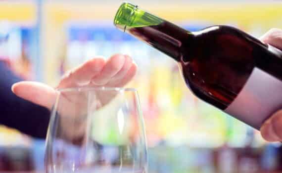 A restaurant patron puts a hand over his wine glass to stop a waiter from filling it.