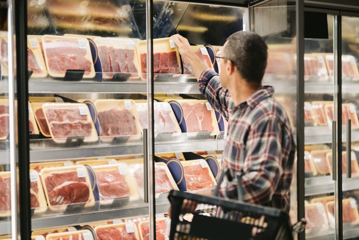 Male customer with a shopping basket taking meat from a fridge at local supermarket