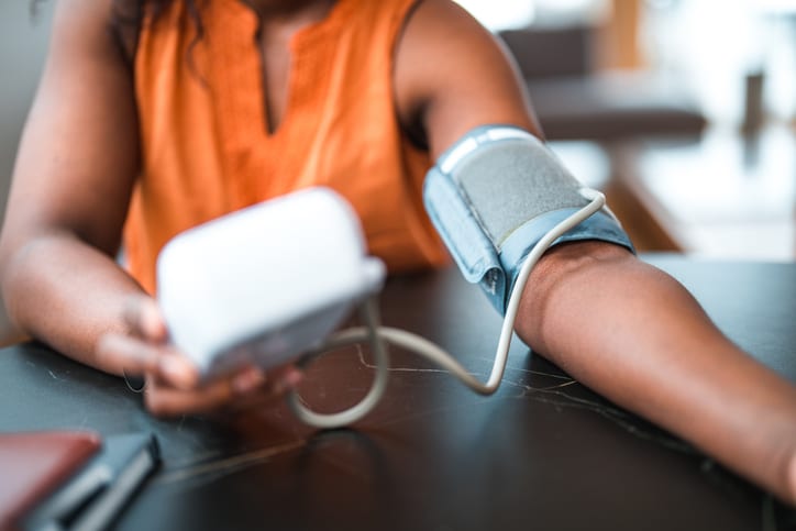 Close up on hands of a mid adult black female using a medical device in a domestic dining room. Measuring blood pressure at home.