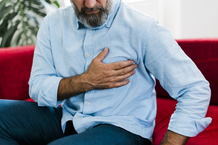 Senior man feeling unwell, suffering from backache, massaging aching muscles while sitting on sofa in the living room at home. Elderly and health issues concept