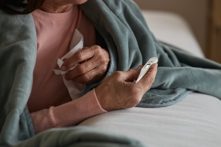 A woman wrapped in a shawl checks her temperature on a thermometer.