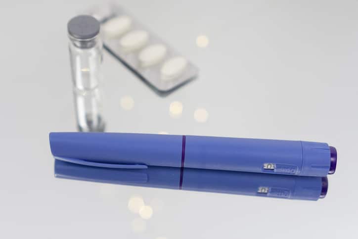 Ozempic semaglutide injection pen on reflective surface with blurred medicine bottle and pills concept of diabetes medication, weight loss treatment, pharmacy, and healthcare.