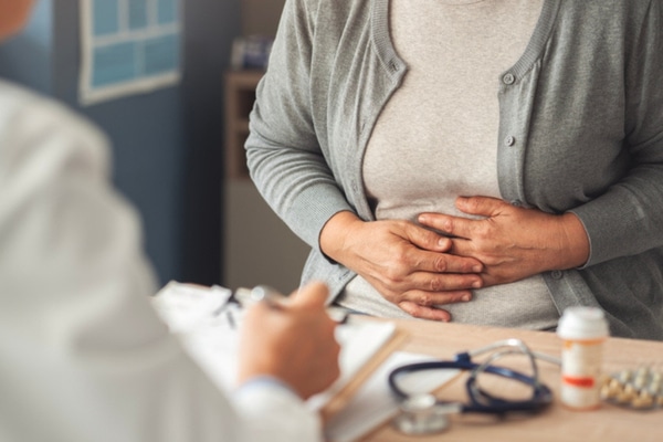 Woman holds stomach while talking to doctor