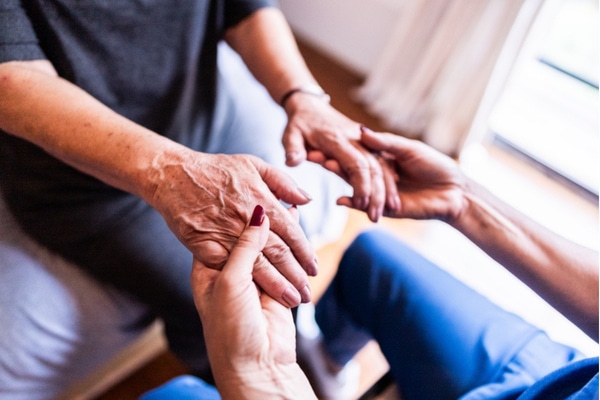 A home health aide holds the hands of a patient with Parkinson's disease.