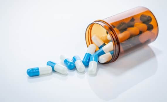 Prescription antibiotic capsules spilling from amber bottle on white background. Blue and white capsule pills