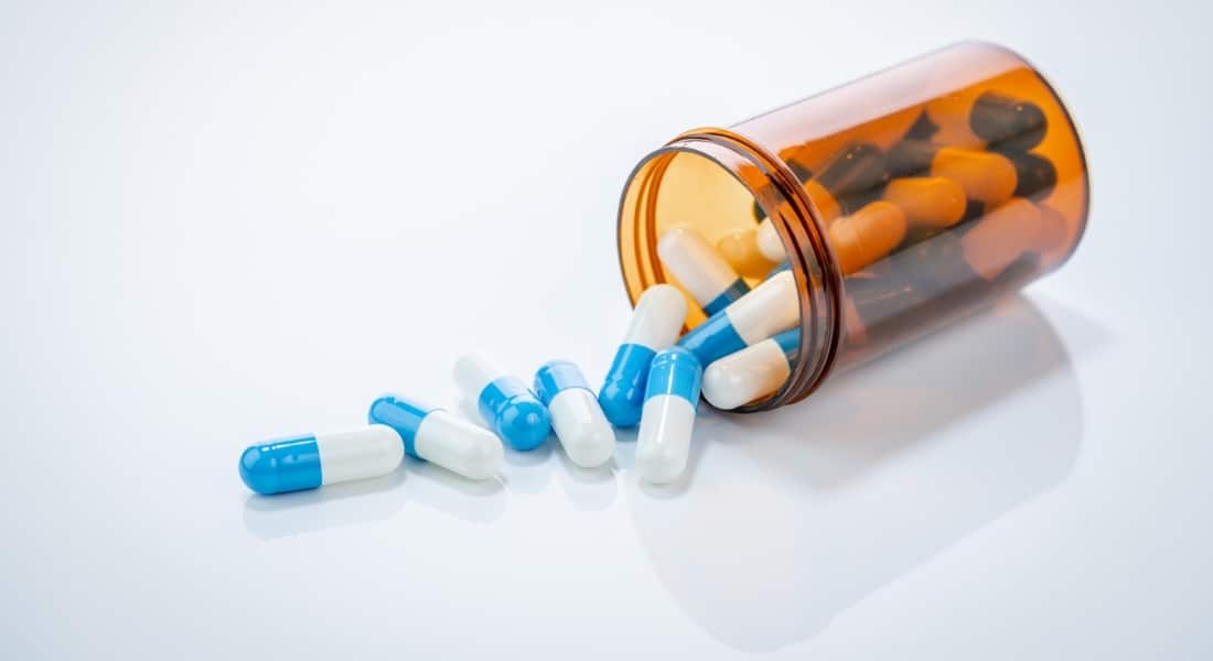 Prescription antibiotic capsules spilling from amber bottle on white background. Blue and white capsule pills