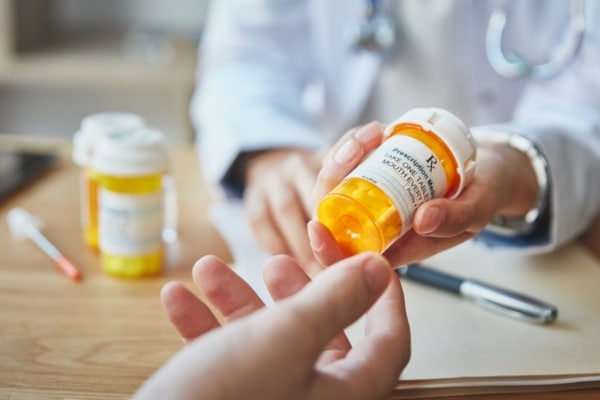 A doctor hands a prescription bottle of antibiotics to a patient.