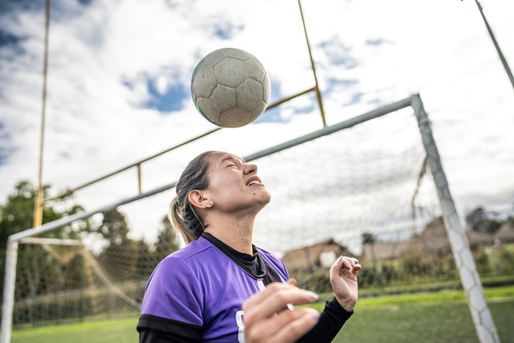 Soccer player mid adult woman heads ball on soccer field