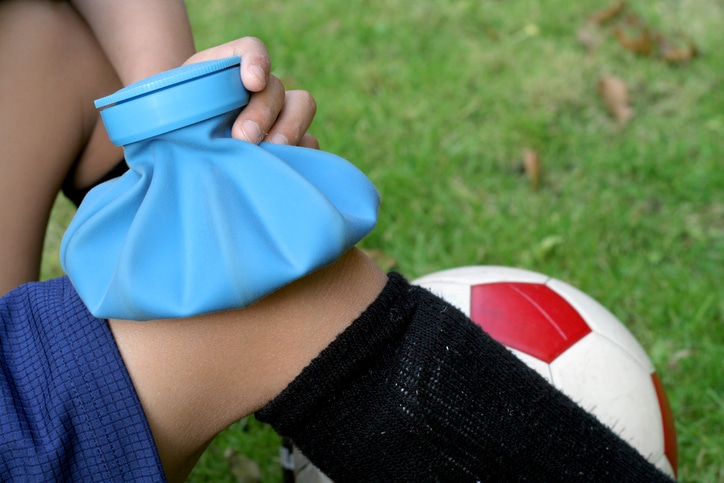 A young soccer player with a knee injury holding an ice bag over it.