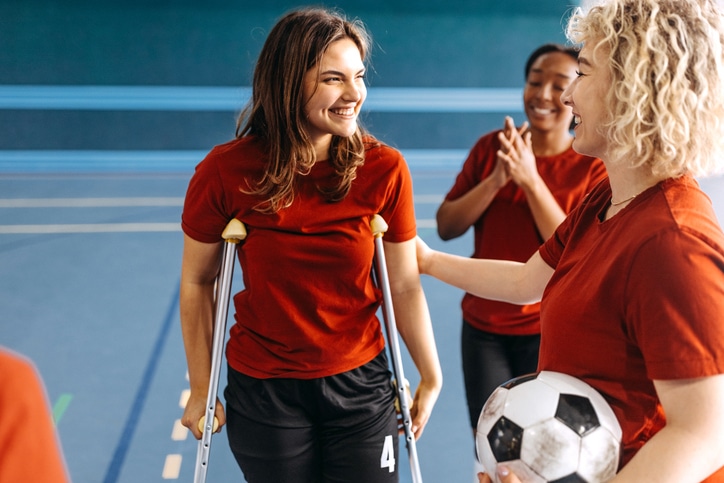 Teenage female soccer player coming back to the team with crutches after an injury