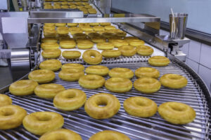 Freshly baked donuts coming out of a conveyor belt.