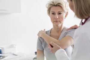 Doctor assisting mature patient in stretching her arm at hospital