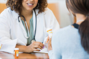 An unrecognizable female patient holds a prescription medication container as she discusses the medication’s instructions and side effects with a female doctor.