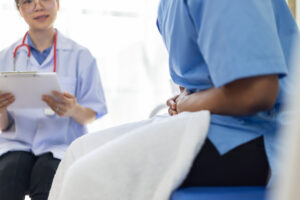 A female doctor talks to a young Asian woman about her stomach pain at the clinic table.