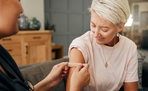healthcare worker and elderly woman with a bandaid on her arm after a treatment in a nursing home