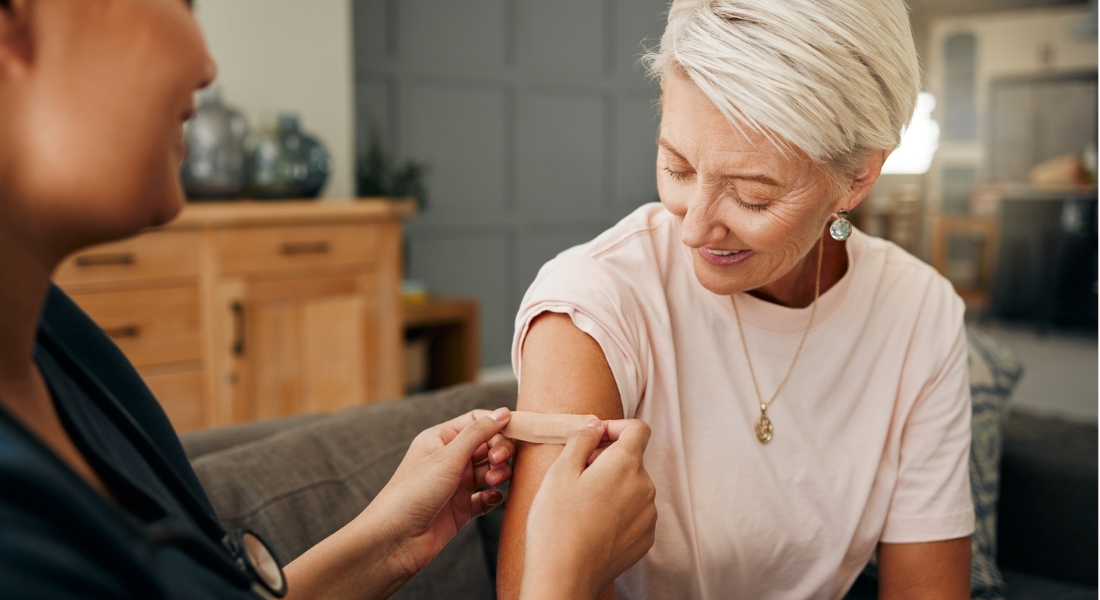healthcare worker and elderly woman with a bandaid on her arm after a treatment in a nursing home