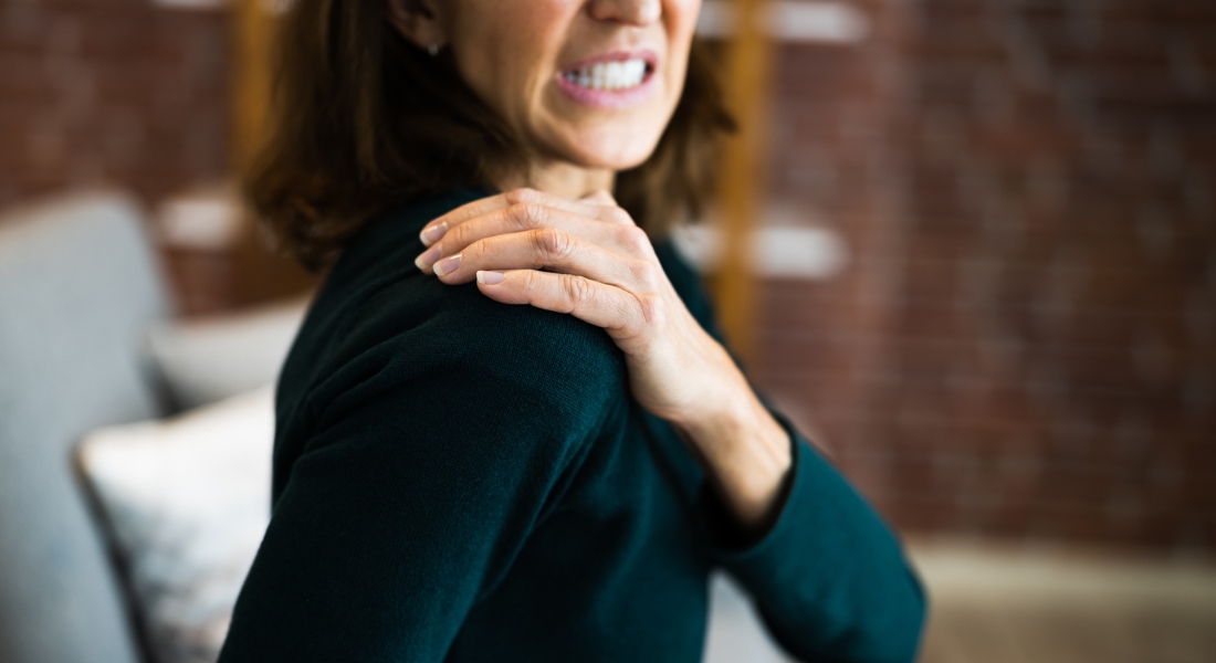 A woman grimaces while suffering from frozen shoulder.