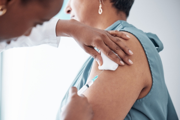 Medicine, healthcare and doctor with woman for vaccination in a clinic for medical treatment for prevention. Closeup of a nurse doing a vaccine injection with a needle syringe in a medicare hospital.