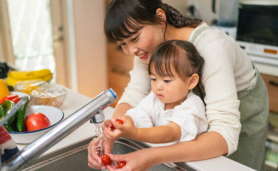A mother is helping her small daughter washing vegetables and encouraging her for healthy eating.